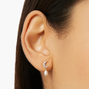 Detailed close-up of a gold moon-shaped earring with crystals and a white pearl on ear