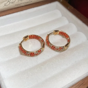 Close-up of gold circle earrings with orange and white zircons in a jewelry box