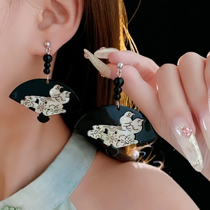 Detailed view of fan-shaped black earrings with white bird patterns on a model
