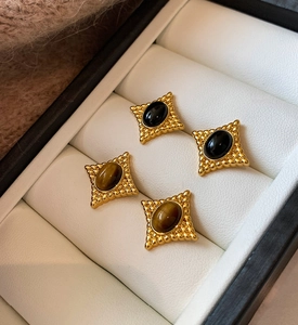 Détail de boucles d'oreilles vintage en or avec pierre œil de tigre dans un écrin en cuir blanc