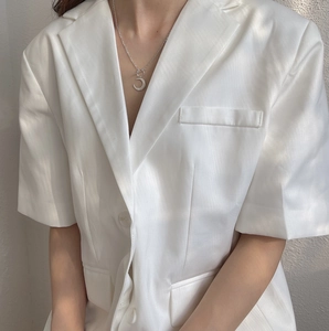 Detail of a matte silver crescent moon necklace worn with a white silk blazer