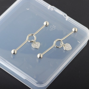 Close-up of silver industrial barbell piercing jewelry with heart pendant and crystals