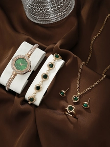 Elegant gold jewelry set with green heart stones and pearl watch on brown silk