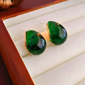 Detail of vintage teardrop earrings with green resin stone and gold-plated metal base