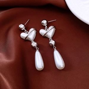 Detail of vintage silver pearl heart earrings on elegant dark red silk fabric