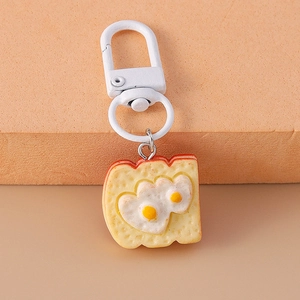 Detail of toast keychain with heart-shaped fried eggs on a soft textured background