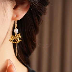 Detail of a gold rocking horse earring with a pearl on a model with warm background