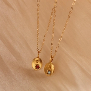 Detail of gold titanium necklaces with initial pendants E and A featuring zircon gemstones