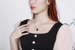 Detail of a minimalist gold necklace with a round embossed letter pendant on a model