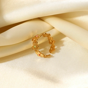 Bague fleur en acier doré 18k avec émail coloré présentée sur un tissu en soie beige