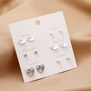 Detailed view of 6 pairs of silver earrings with whale and heart motifs on a pink card
