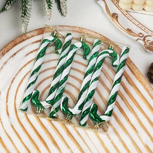 Close-up of green and white glitter candy cane ornaments on a snowy wooden tray for Christmas