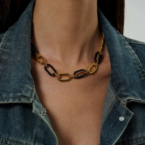 Dettaglio di una collana a catena spessa oro e nero indossata su una giacca di jeans