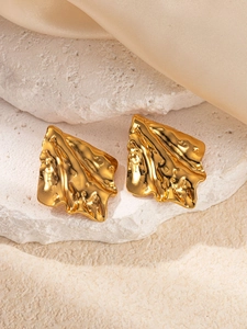 Detail shot of golden crumpled metal stud earrings on white stone and silk fabric