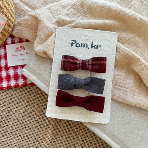 Three-piece fabric bow hair clips in red plaid, grey, and maroon on a display card