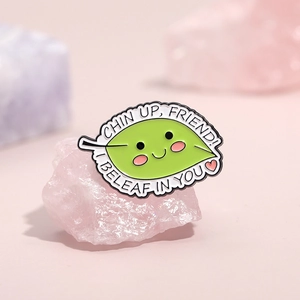 Cute green leaf enamel pin with inspirational text on a pink crystal background