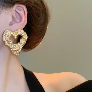 Close-up of golden hollow heart earrings with molten lava texture on female model