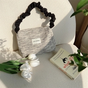 Close-up of textured tweed tote bag with ruffled handle and branded logo patch on sofa