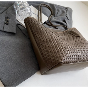 Detailed view of dark brown woven tote bag with professional gray blazer on white background