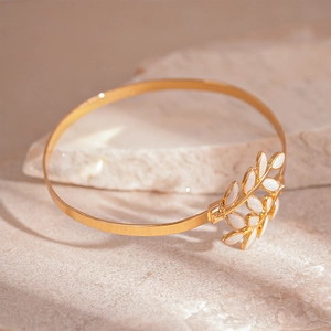 Minimalist gold leaf open cuff bracelet with white enamel on natural stone background