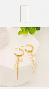Macro detail of golden bamboo hoop earrings with baroque pearls and metal tassels