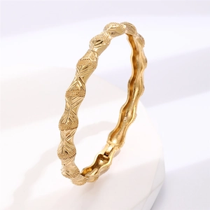 Macro detail of gold plated geometric bangle showing intricate embossed floral textures