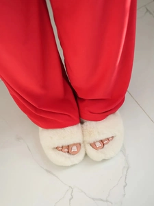 Close-up of white plush open-toe faux fur slippers worn with red pajama pants