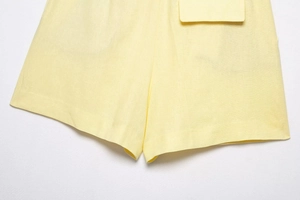 Detailansicht der gelben Leinen-Shorts zeigt Stofftextur und Nähte der Tasche