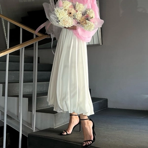 Detail van witte geplooide midi-rok met elegante drapering en zwarte sandalen met hak