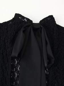 Detail of elegant black lace top featuring a large satin bow tie back and hollow texture
