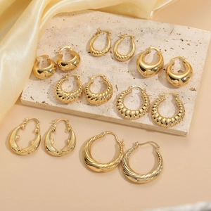 Close-up of seven pairs of gold plated brass hoop earrings on a beige stone slab background