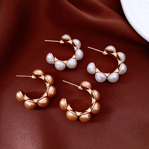 Détail de boucles d'oreilles C dorées avec perles blanches et champagne sur du satin