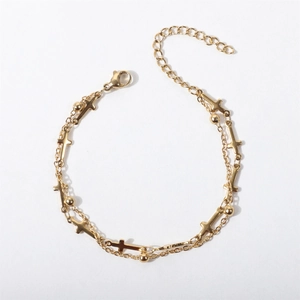 Detailed view of a gold double-layer chain bracelet with cross charms and beads on white