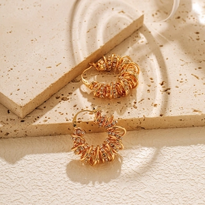 Gold plated spring wire hoop earrings with zircon accents on a textured stone background