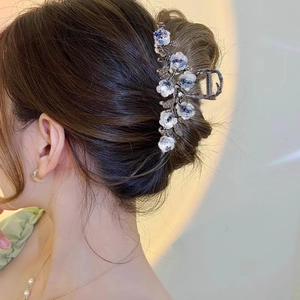 Détail de la pince à cheveux camélia bleu et blanc avec strass sur un chignon brun
