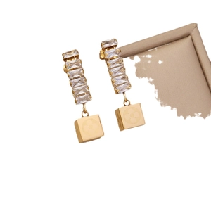 Golden earrings with clear crystals and clover pattern square pendants on white background