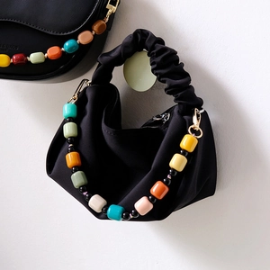 Detail of colorful candy bead chain on black satin pleated bag handle with gold accents