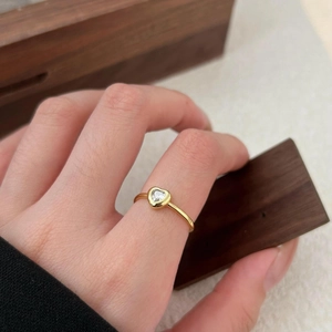 Close-up of a heart-shaped zircon ring with a minimalist gold band worn on a finger