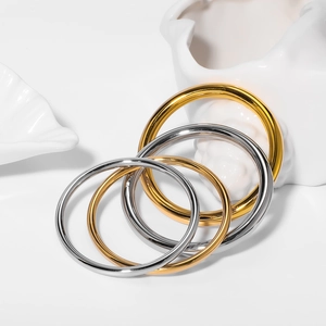 Minimalist 18k gold and silver stainless steel bangles set on a decorative white shell