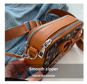 Detail view of smooth dual zippers and brown bow accent on leopard print crossbody bag