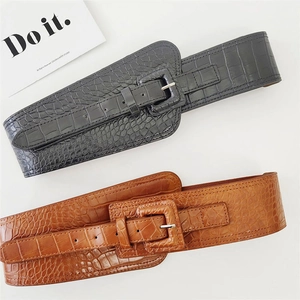 Flat lay of wide crocodile pattern corset belts in black and brown with large pin buckles