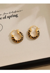 Detail of 14k gold plated leopard print hoop earrings with enamel finish on beige canvas