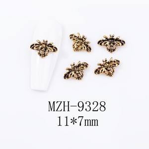 Macro detail of 11x7mm vintage gold alloy bee nail art charms on a white manicure tip