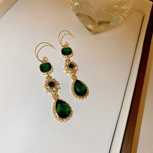 Macro detail of emerald green drop earrings with vintage gold settings and zircon stones