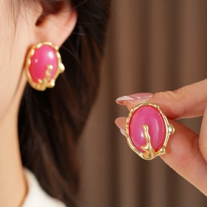 Gros plan de boucles d'oreilles dorées texturées avec résine rose portées par un modèle