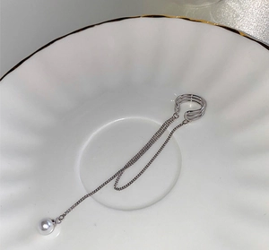 Detail shot of silver fringe ear cuff with artificial pearl on a white ceramic dish