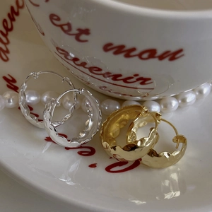 Macro shot of wavy S925 sterling silver hoop earrings displayed on a white porcelain dish