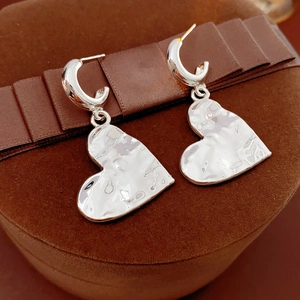Detail of silver heart-shaped pendant earrings with hammered texture on a gift box