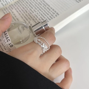 Detail of silver irregular lava texture ring and beaded chain ring worn on hand