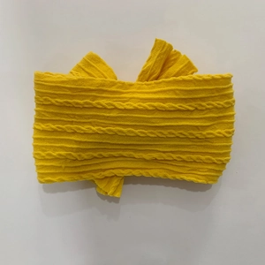 Detail of yellow knit baby headband featuring a large bow and cable knit texture